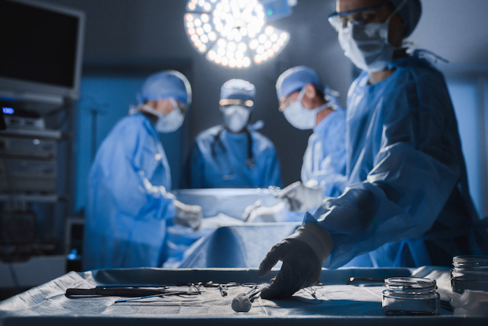 Surgical tools lying on table while group of surgeons at background operating patient in surgical theatre
